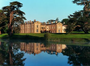 Exterior view of Compton Verney building behind a lake, surrounded by tall trees on a sunny day